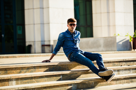 street fashion. fashionable man in jeans outfit, outdoor posing on stairsの写真素材