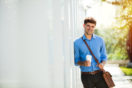 handsome young man  with coffee leaning on a wall before going to office in a sunny dayの写真素材