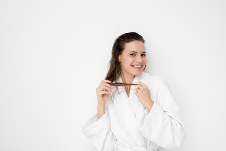 happy young and natural woman standing in bathrobe after a shower, playing with her wet hair and smilingの写真素材