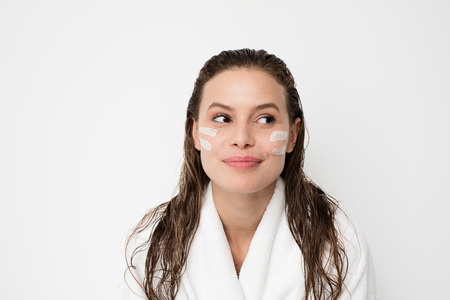 portrait of young woman with two lines of cream skin treatment on her face, smiling to camera with...