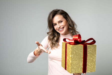 beautiful woman in pink sweater presenting her golden gift to camera on gray backgroundの写真素材