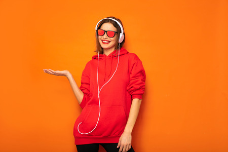 young and rebel girl in red hoodie with headphones and sunglasses listening music, cool hipsterの写真素材