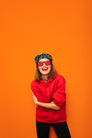young and cool hipster girl having fun, with colored hat and sunglasses posing with good vibes to camera on orange backgroundの写真素材