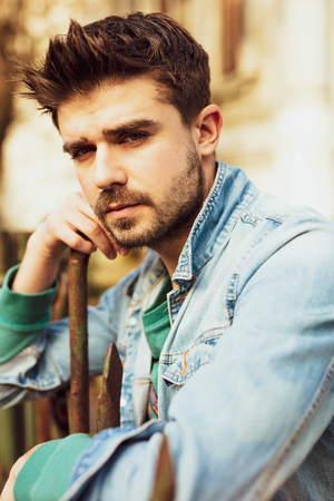 handsome guy in jeans jacket standing on a metal fenceの写真素材