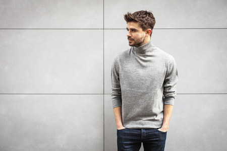 elegant and stylish man with hands in pockets standing on a gray wallの写真素材