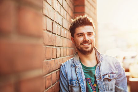 handsome and cool young man posing against a brick wall and smiling to camera, lifstyle picture with a modern studentの写真素材