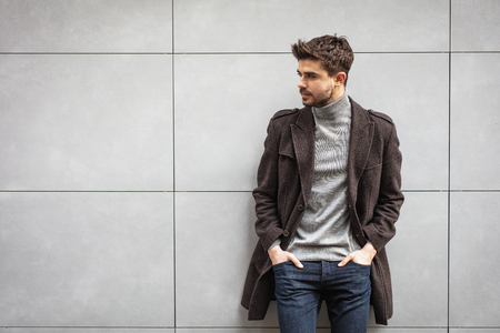 young attractive man in coat posing on a grey wall , stylish manの写真素材