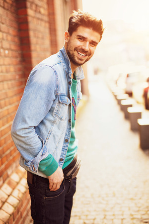 lifstyle picture with a young and modern man walking on the street with a positive atittude, smiling, cross to a brick wallの写真素材