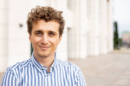 portrait of a young and happy man with blonde and curly hair smiling and inspiring success