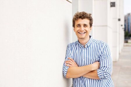 smart casual man standing against a white wall of a buiding looking with confidence to cameraの写真素材
