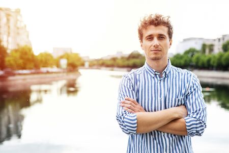 young man smart casual dressed looking with confidence to camera having a river behind, standing with arms crossedの写真素材