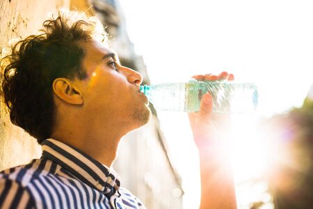 hot summer days in the city, young man drinking a bottle of waterの写真素材
