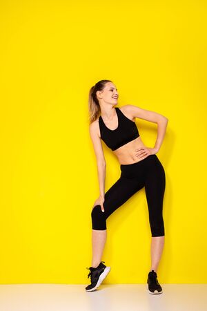 young and athletic woman in sportwear smiling and being happy of her body and her lifestyle on yellow backgroundの写真素材