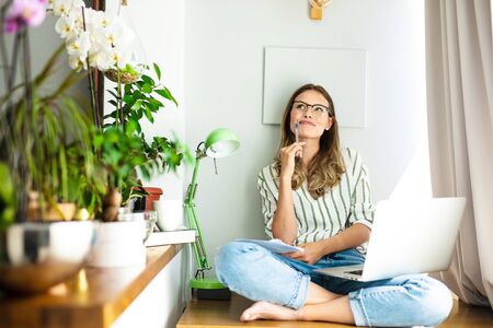 work from home or studding online, concept with a woman working at laptop inside the house, next to a bright window and the houseplantの写真素材