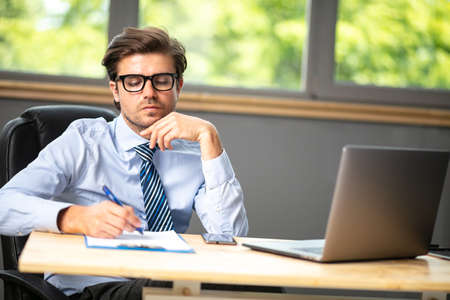 concerned elegant businessman, sitting at his office and looking focused and worried, talking with someone on cellphoneの写真素材