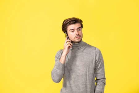 portrait of a young man using his cellphone on yellow background