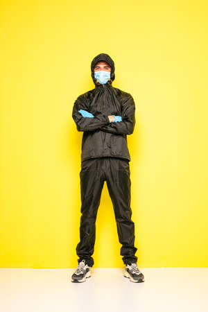 isolated man on yellow background in full body black costume, with medical mask and steril glovesの写真素材
