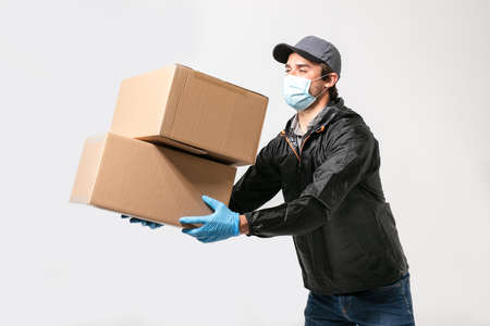 delivery man wearing medical protection against infection, carrying a package on grey backgroundの写真素材