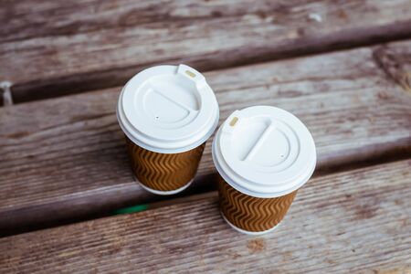 Two paper cup of coffee on wooden background. Coffee stands on a bench on the street. Romantic date with coffee. Business meeting. Nice conversation over a cup of coffee.の写真素材