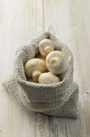 Champignon mushrooms in canvas bag on wood textureの写真素材