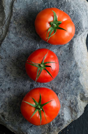 Three tomatoes over dark gray stone, above viewの写真素材