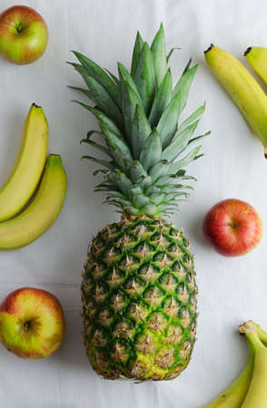 Pineapple, apples and bananas over white cloth, above viewの写真素材