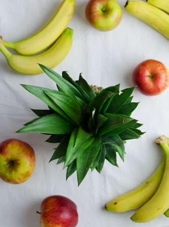 Pineapple, apples and bananas over white cloth, above viewの写真素材