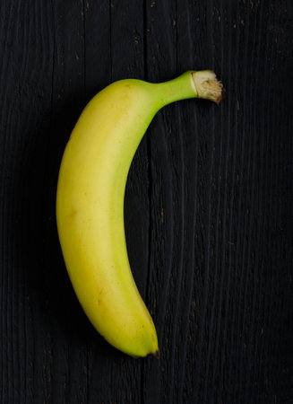 Single bananas over black wooden table, above viewの写真素材