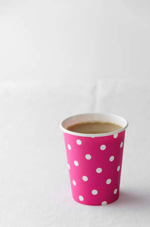 Coffee in a pink paper cup with dots pattern over white clothの写真素材