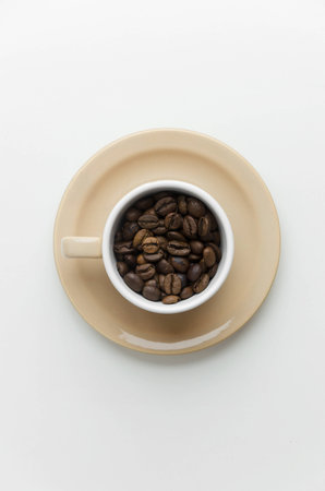 Coffee beans in a cup over white table, above view