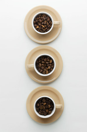 Coffee beans in cups over white table, above view