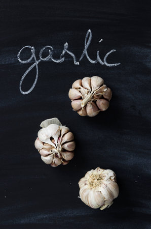 Cloves of garlic over black chalkboard with handwritten word garlic, above view