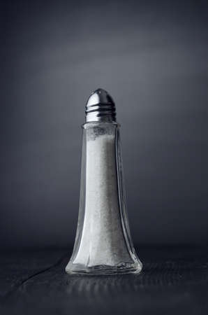 Close up of a salt shaker over black wooden tableの写真素材