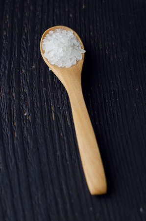 Close up of a spoon with salt over black wooden tableの写真素材
