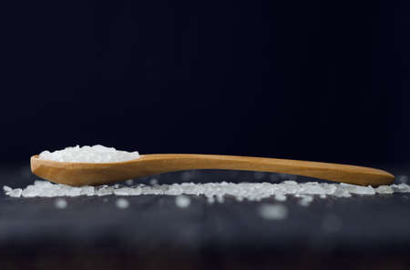 Close up of a spoon with salt over black wooden tableの写真素材