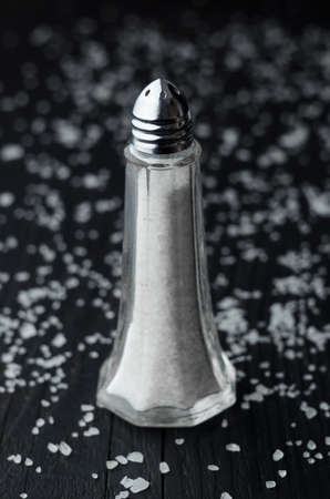 Close up of salt shaker over black wooden table with salt all over itの写真素材