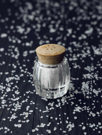 Rustic salt shaker over black wooden table with salt all over it
