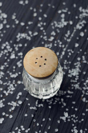 Rustic salt shaker over black wooden table with salt all over itの写真素材
