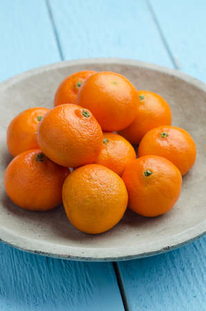 Multiple clementines in a rustic ceramic bowl over blue wooden tableの写真素材