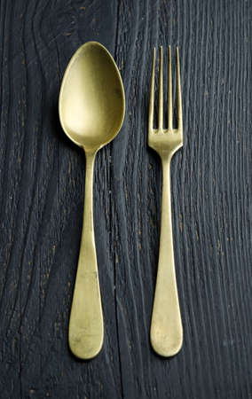 Golden spoon and a fork over black wooden table, top viewの写真素材