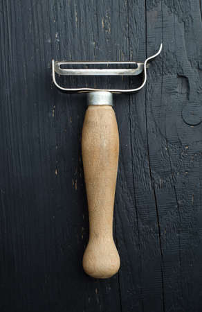 Wooden potato peeler close up over black wooden table, above viewの写真素材