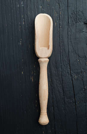 Small wooden scoop close up over black wooden table, above view.の写真素材