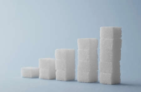 Concept: Ascending stacks of sugar cubes over blue background. This in a concept for high risk of...