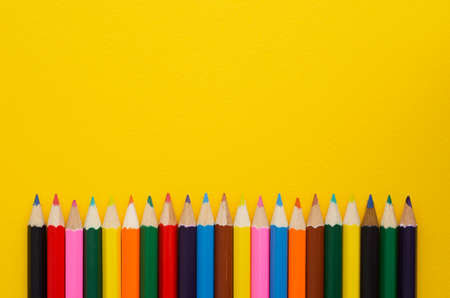 Colorful crayons organized in a row over yellow background, above view with copy space for text or other designの写真素材