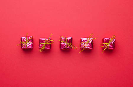 Small Red Christmas Gift Boxes organized in a row over red background, above viewの写真素材