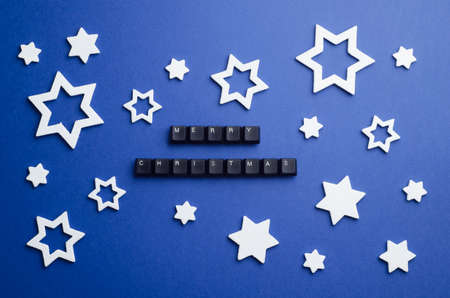 Merry Christmas text made of keyboard keys and other christmas white stars decoration over dark blue background, above viewの写真素材