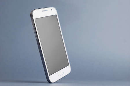 White Smart Phone tilted over dark blue gray background. Clipping path around the phone screen.の写真素材