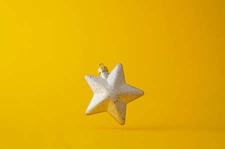 Silver christmas star floating in the air over bright yellow background with copy spaceの写真素材