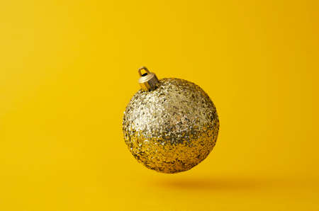 Glitter golden christmas ball floating in the air over bright yellow backgroundの写真素材