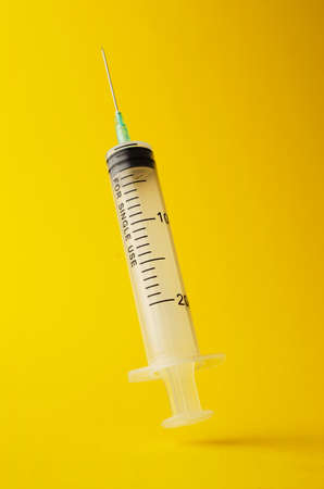 Syringe floating in the air over bright yellow backgroundの写真素材